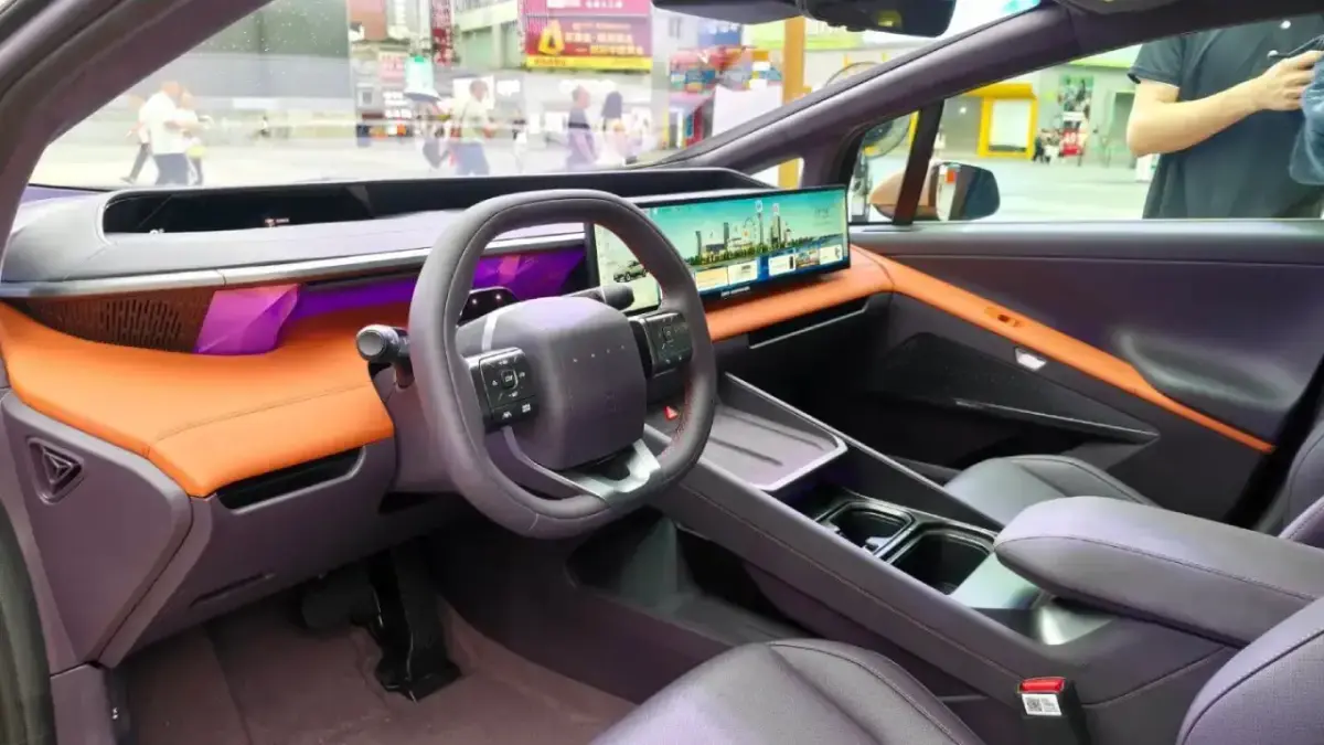 Das futuristische Cockpit des Hyundai IONIQ V mit einem extrem breiten Widescreen-Display und leuchtend orangen Leder-Akzenten. Zu sehen sind das abgeflachte Lenkrad und eine lila Ambientebeleuchtung Das futuristische Cockpit des Hyundai IONIQ V mit einem extrem breiten Widescreen-Display und leuchtend orangen Leder-Akzenten. Zu sehen sind das abgeflachte Lenkrad und eine lila Ambientebeleuchtung
