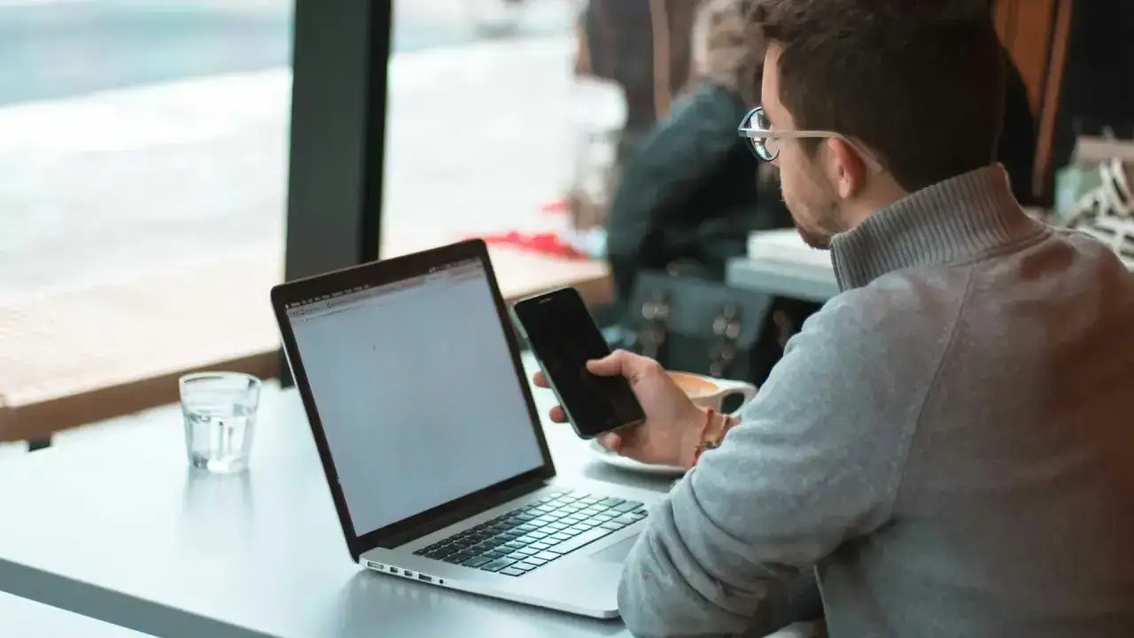Mann sitzt mit Laptop und Smartphone am Fenster an einem Tisch