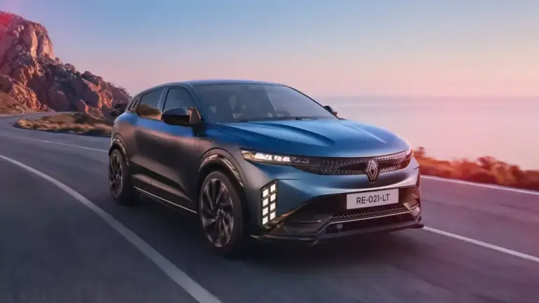 Der vollelektrische Renault Scenic E-Tech in Dunkelblau fährt dynamisch auf einer malerischen Küstenstraße im Sonnenuntergang. Das moderne Familien-E-SUV zeigt seine markante Front mit dem neuen Rauten-Design
