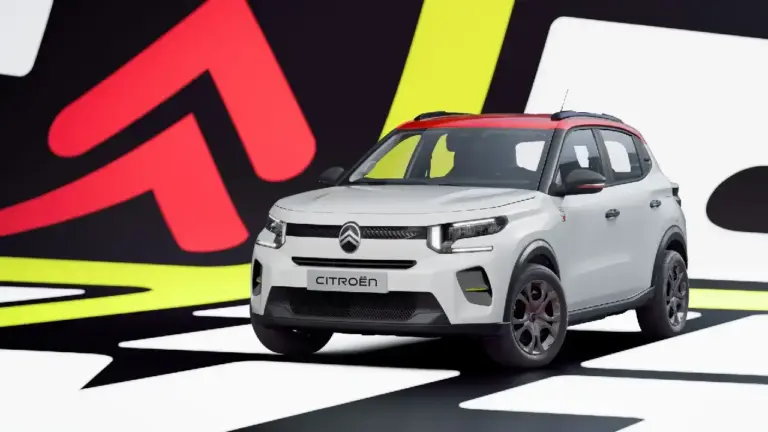 Schräge Frontansicht des elektrischen Citroën ë-C3 in Weiß mit rotem Kontrastdach. Der günstige Elektro-Kleinwagen zeigt sein C-förmiges LED-Lichtdesign vor einer bunten Pop-Art-Kulisse
