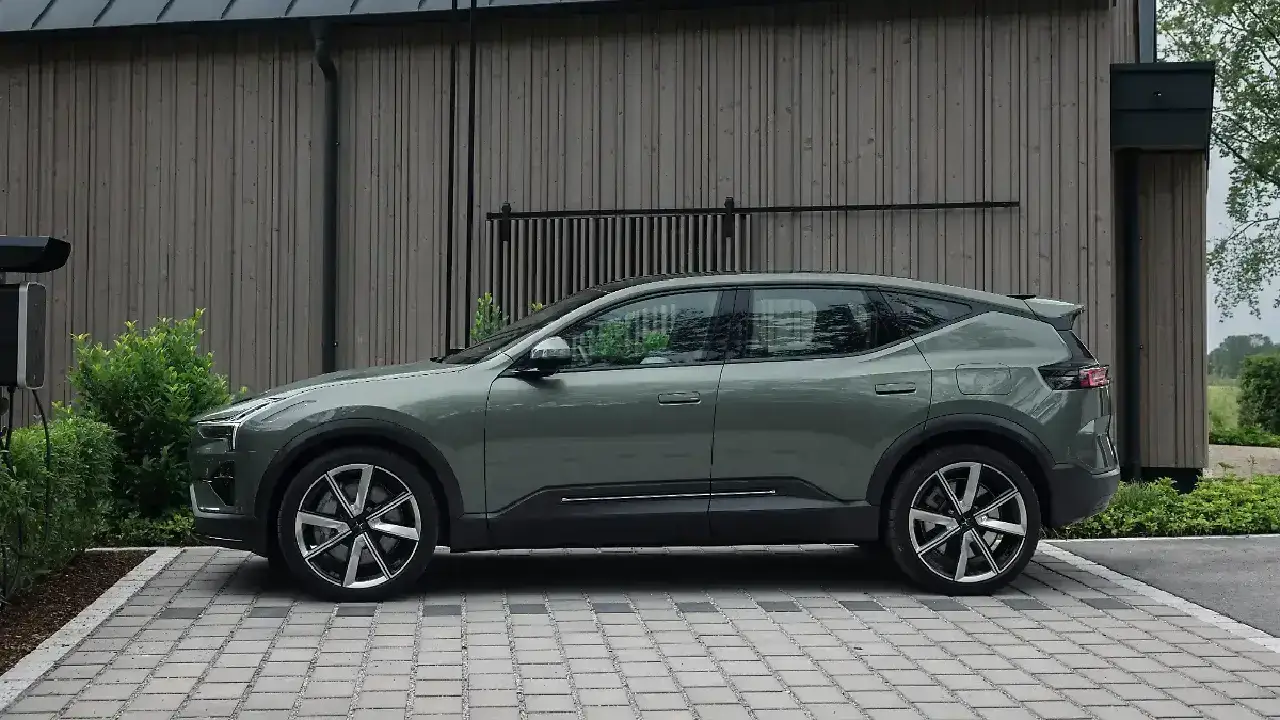 Seitenansicht des Polestar 3 800V SE Elektro-SUVs in Salbeigrün beim Ladevorgang an einer Wallbox. Die Profil-Ansicht zeigt die coupéhafte Linienführung und sportliche 7-Speichen-Felgen vor einer modernen Holzfassade